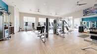 Located at 1291 S Ulster St in Denver, CO, this state-of-the-art fitness center and yoga studio offers a generously sized, single-floor facility designed to support a full range of workout disciplines. The space features light-toned hardwood-style flooring laid in a herringbone pattern throughout, complementing the clean, neutral-toned walls and bright recessed lighting overhead. Multiple ceiling fans ensure consistent air circulation across the entire floor.

The main exercise area is outfitted with an extensive selection of strength training equipment, including multi-station cable machines, weight benches, and a dumbbell rack, alongside a variety of cardio machines such as treadmills, ellipticals, stationary bikes, and a rowing machine. Exercise balls and functional training accessories are neatly organized along the walls. Large wall-mounted mirrors expand the sense of space and support proper form during workouts.

A dedicated yoga and studio section features open floor space, floor-to-ceiling mirrors, a wall-mounted television, and a built-in computer workstation — ideal for guided classes or personal training sessions. This area also benefits from a dramatic glass garage-style door that opens to an outdoor view, flooding the space with natural light. A wall-mounted mini-split climate control unit ensures year-round comfort. Oversized windows throughout the facility invite ample daylight, creating an energizing and welcoming workout environment.