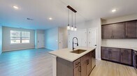 This single-floor residence on Whiskey Way in Ballston Spa, NY offers a well-designed layout across two bedrooms and one bathroom. The open-concept kitchen and living area serves as the heart of the home, anchored by a central island with a light quartz countertop, an undermount sink, and a matte black industrial-style faucet. Three pendant lights hang above the island, adding character to the space. Rich, dark wood cabinetry lines the kitchen walls, complemented by a white herringbone tile backsplash and stainless steel appliances, including a range, over-the-range microwave, and a French door refrigerator. Light wood-style plank flooring runs throughout the main living areas, contributing to a bright and cohesive aesthetic.

The primary bedroom offers a generous footprint with soft carpeting and natural light from a large window. The second bedroom features similar light flooring and a window overlooking the neighborhood. The bathroom is finished with a floating wood-toned vanity, a light quartz countertop, an undermount sink, matte black fixtures, and a large framed mirror. Neutral wall tones and clean white Shaker-style doors are consistent throughout, creating a modern, move-in-ready atmosphere.