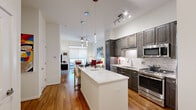 This single-floor, one-bedroom, one-bathroom unit is thoughtfully designed to maximize its compact footprint. The open-concept kitchen and living area form the heart of the space, anchored by rich hardwood flooring that runs throughout. The kitchen is a standout feature, showcasing floor-to-ceiling dark espresso cabinetry, marble-patterned countertops, a full suite of stainless steel appliances including a gas range, built-in microwave, dishwasher, and French door refrigerator, plus a subway tile backsplash. A peninsula island with a white quartz surface offers additional prep space and seating, illuminated by elegant pendant lighting above.

The living area benefits from tall ceilings, a ceiling fan, and large sliding glass doors that open to a private balcony, allowing ample natural light. The bedroom is a quiet retreat featuring a wide window with roller shades and cozy carpeting. The bathroom is finished with marble-look tile flooring and walls, a glass-enclosed walk-in shower, granite vanity countertop, and gray cabinetry, delivering a clean, contemporary aesthetic throughout.