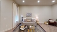 This single-floor residence showcases a thoughtfully designed layout with modern finishes and a cohesive neutral color palette throughout. The open-concept kitchen is a standout feature, outfitted with crisp white shaker cabinetry extending to the ceiling for ample storage, granite countertops, and a full suite of stainless steel appliances including a French door refrigerator, built-in microwave, and range. A large central island with an undermount sink and additional seating space anchors the kitchen, illuminated by a trio of elegant gold-accented pendant lights. Light wood-look flooring ties the kitchen and entry areas together seamlessly. The living area offers a comfortable and inviting atmosphere, featuring recessed lighting, large windows dressed with sheer white curtains that allow natural light to flow in, and views of the surrounding exterior. The bedroom continues the warm, neutral tone with soft carpeting, generous window placement offering outdoor views, and ample space for furnishings. The bathroom is finished with granite countertops, white cabinetry, a framed mirror, globe vanity lighting, and a shower-tub combination. Throughout the residence, clean architectural lines, arched interior doorway details, and consistent high-quality finishes create a polished and comfortable living environment.