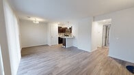This well-appointed 2-bedroom, 1-bathroom single-floor residence offers a thoughtfully designed layout with a clean, modern aesthetic throughout. The open-concept living and kitchen area serves as the heart of the unit, featuring durable wood-style flooring that runs seamlessly throughout the main areas. The kitchen is equipped with dark cabinetry, stainless steel appliances including a refrigerator and microwave, and a peninsula with a light-toned countertop that provides additional prep and dining space, accented by a pendant light overhead. The living area is bright and airy, highlighted by a sliding glass door with vertical blinds that opens to a private balcony with outdoor views. Both bedrooms are carpeted and include ceiling fans with integrated lighting. The primary bedroom offers a comfortable footprint with a closet, while the second bedroom features a window with natural light. A central hallway connects the bedrooms to the shared full bathroom, which includes a tiled tub-and-shower combination, a dark-cabinetry vanity, and wood-style flooring. A dedicated closet and hallway provide additional storage. The entry door opens into the living space, creating a welcoming transition into the home.