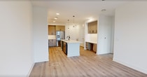 This thoughtfully designed 1-bedroom, 1-bathroom apartment offers 650 square feet of modern living space on a single floor. The open-concept kitchen and living area serves as the heart of the unit, featuring light wood-tone cabinetry, stainless steel appliances, a built-in microwave, and a sleek central island with a white quartz countertop and pendant lighting overhead. A built-in desk nook adds functional workspace off the main living area. Recessed lighting and light hardwood-style flooring run throughout, creating a bright, cohesive aesthetic. The 130-square-foot primary bedroom is airy and well-lit, equipped with a ceiling fan and large windows offering outdoor views. French doors lead to a private balcony with scenic surroundings. The bathroom is a standout, finished with a bold blue vanity, white quartz countertop, backlit mirror, large-format tile flooring, and a tall linen cabinet for added storage. A dedicated closet completes the unit. Clean white walls, black hardware accents, and contemporary finishes give this apartment a polished, modern character throughout.