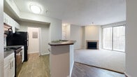 This single-floor, 2-bedroom, 2-bathroom residence offers a thoughtfully designed layout that maximizes functionality and comfort. The combined kitchen and living area serves as the heart of the home, where wood-look flooring flows through the kitchen and transitions to plush carpeting in the living room. The kitchen features white cabinetry, dark countertops on a peninsula breakfast bar, and black appliances, offering a practical and stylish workspace. The living room is anchored by a tile-surround fireplace and a full-width sliding glass door with vertical blinds, allowing natural light to fill the space and providing direct access to the outdoors.

Both bedrooms are carpeted and finished with neutral tones, offering a calm and restful atmosphere. The primary bedroom is generously sized and includes a walk-in closet equipped with dual hanging rods and built-in shelving for ample storage. The second bedroom benefits from a large window with outdoor views. Each bathroom includes a tiled tub-shower combination in a clean, all-white finish. Additional highlights include a utility room, a hallway connecting all areas, and textured ceilings throughout, contributing to the home's cohesive and practical design.