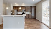 This two-story residence is designed with a clean, contemporary aesthetic and a practical layout across both levels. The main floor opens with a dramatic two-story entryway, where soaring ceilings draw the eye upward and clerestory windows flood the space with natural light. A built-in cabinet niche and carpeted staircase add functional character to the foyer, while wood-look vinyl flooring extends throughout the main living areas.

The open-concept kitchen and living area form the heart of the main floor. The kitchen is outfitted with rich, dark-stained cabinetry extending to the ceiling for ample storage, stainless steel appliances including a range, microwave, and refrigerator, and a white quartz peninsula with bar seating. French doors and large windows at the rear of the living space invite natural light and outdoor views. A half bathroom is conveniently located on this level.

Upstairs, carpeted bedrooms offer a comfortable retreat, each with natural light from windows. The upper-level hallway features a wood handrail and leads to a walk-in closet and a full bathroom complete with a single-sink vanity, white quartz countertop, wood-toned cabinetry, and a glass-enclosed walk-in shower with wood-look flooring.