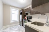 Located at 42 Maitland St in Toronto's vibrant Church-Wellesley neighbourhood, this well-appointed unit offers three bedrooms, a living room, a kitchen, and a hallway across a single floor. The space blends classic architectural character with functional updates throughout.

The living room serves as a focal point, showcasing a striking wood-mantled fireplace with dark tile surround, original crown moulding, and tall white-trimmed windows — including one with charming leaded glass detail — that bring in natural light. Rich dark hardwood flooring runs throughout the main living and bedroom areas, reinforcing a warm, cohesive aesthetic.

The three bedrooms are efficiently laid out, each featuring white-trimmed windows, classic baseboard moulding, and neutral grey walls. Several rooms include glass-panelled interior doors with transom windows above, adding an elegant, period-appropriate touch. Cast iron radiators are present, reflecting the building's heritage character.

The kitchen has been modernized with dark wood-grain cabinetry, white quartz countertops, a white tile backsplash, stainless steel appliances including a refrigerator and range, and a classic black-and-white mosaic tile floor. A window above the counter allows natural light into the cooking space.

Overall, the unit presents a thoughtful combination of heritage architectural details and contemporary finishes.