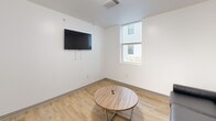 Located at 815 S Aurora St in Ithaca, NY, this 2-bedroom, 1-bathroom unit offers a clean, modern design across a single floor. The open-concept kitchen and living area serves as the heart of the space, featuring white shaker cabinetry, stainless steel appliances including a refrigerator, electric range, and over-the-range microwave, and a peninsula with bar seating and pendant lighting. Light wood-look flooring runs throughout the common areas, adding warmth to the bright, white interior. The living room provides a comfortable gathering space with a wall-mounted TV, round coffee table, and a window that brings in natural light. The two bedrooms feature carpet flooring and private entry doors, each accommodating a bed and offering a functional layout. One bedroom includes a window with an exterior view and a built-in desk area. The bathroom is finished with the same light wood-look flooring, maintaining a cohesive aesthetic throughout the unit. The overall design is contemporary and practical, with a clean, neutral palette that creates a bright and functional living environment.