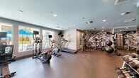 Located in Escondido, CA, this fitness center offers a well-appointed, single-floor exercise space designed to support a full range of workout routines. The room is finished with durable rubberized flooring throughout, providing a safe and practical surface for all types of physical activity.

A standout design feature is the bold camouflage-patterned accent wall, which adds a dynamic visual element to the space. Full-length mirrors are strategically placed along the walls, enhancing the sense of openness while allowing users to monitor their form during workouts.

The cardio zone is positioned along a windowed wall that looks out toward a pool area with umbrella-shaded seating, filling the space with natural light and pleasant outdoor views. Equipment in this area includes treadmills, elliptical trainers, a stationary bike, and a rowing machine.

The strength training section is comprehensively outfitted with a multi-station cable and weight machine, a dedicated dumbbell rack with a full range of free weights, medicine balls, stability balls on a tiered rack, a punching bag, and TRX suspension trainers mounted to the wall.

Recessed lighting provides consistent, even illumination throughout the room, while ceiling-mounted HVAC vents ensure a comfortable environment. The fitness center is accessible via a stairwell and is well-suited for residents seeking a convenient, fully equipped space for daily exercise.