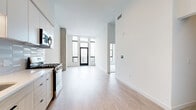 Located at 328 W 12th Ave in Denver, CO, this modern 1-bedroom, 1-bathroom residence offers a thoughtfully designed layout with high-end finishes throughout. The open-concept living and kitchen area is anchored by light wood-tone flooring, soaring ceilings, and floor-to-ceiling windows that flood the space with natural light and frame striking city views. Exposed concrete columns add an industrial character that complements the contemporary aesthetic.

The kitchen is well-appointed with two-tone cabinetry — crisp white uppers paired with warm wood-grain lowers — a subway tile backsplash, stainless steel appliances including a gas range and dishwasher, and ample counter space. A hallway entry with high ceilings leads seamlessly into the main living area, with a distinctive blue front door providing a bold accent.

The bedroom features plush carpeting, a large picture window with expansive views of the Denver skyline, and generous closet space. The bathroom is finished with large-format gray tile surrounding a soaking tub, matte black fixtures, and wood-look flooring. Additional conveniences include an in-unit laundry area, a den for flexible use, and a private balcony perfect for enjoying Colorado's outdoor lifestyle.