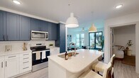 Located in Charleston's historic 29403 zip code, this contemporary 2-bedroom, 2-bathroom residence offers a thoughtfully designed single-floor layout. The open-concept kitchen and living area serves as the heart of the home, featuring striking navy and white two-tone cabinetry, quartz countertops, stainless steel appliances, and a central island with an undermount sink. Pendant lighting and light wood-style flooring add warmth to the space. The living room is bright and welcoming, with large black-framed windows and glass doors that flood the room with natural light and provide access to an outdoor area. Exposed concrete ceilings lend an industrial-modern character throughout, complemented by clean white walls and ceiling fans. The generously sized primary bedroom continues the concrete ceiling aesthetic, with large roller-shade windows and ample room to relax. Both walk-in closets feature multi-tier wire shelving systems for organized storage. The primary bathroom is sleek and elongated, showcasing a dual-sink white vanity, a frameless glass walk-in shower, and a dedicated walk-in closet beyond. The second bedroom is bright and minimalist, with natural light and the same light flooring found throughout the residence.
