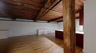 Located at 219 E Bank St in Petersburg, VA, this one-bedroom, one-bathroom loft showcases a compelling blend of historic industrial character and thoughtful modern updates. The open-plan living, dining, and kitchen area is the heart of the home, defined by striking exposed wooden ceiling beams, painted white brick walls, and warm hardwood floors that run throughout the entire space. Exposed black steel piping adds to the industrial aesthetic, while sturdy original timber columns anchor the open layout. The kitchen features rich cherry wood cabinetry, a stainless steel microwave, and ample counter space, flowing seamlessly into the dining and living areas to create a generous, loft-style atmosphere. The bedroom continues the home's signature aesthetic with a full wall of exposed red brick, a wooden beam ceiling, and a window allowing natural light to filter in. The bathroom offers a clean, bright finish with classic white hex tile flooring, a cherry wood vanity with a white countertop, and a large mirror. Additional spaces include a laundry room, a closet, and a utility room, providing practical functionality. This space is a standout example of adaptive historic architecture in the heart of Petersburg.