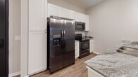 Located in Elkhorn, Nebraska, this single-level studio at Edge 204 offers a thoughtfully designed layout with contemporary finishes throughout. The open-concept kitchen and living area serves as the heart of the space, featuring wood-style plank flooring that extends seamlessly across the main area. The kitchen is well-appointed with white shaker-style cabinetry reaching to the ceiling for ample storage, granite countertops, and a suite of black stainless steel appliances including a side-by-side refrigerator with ice and water dispenser, electric range, and over-the-range microwave. A central island with a granite surface and undermount sink provides additional workspace and casual seating potential, accented by sleek pendant lighting overhead. The living area benefits from a sliding glass door that invites natural light and outdoor views. A separate sleeping area offers carpeted flooring, a ceiling fan, and a window with exterior views. The bathroom includes a full tub and shower combination. A dedicated space accommodates a stacked washer and dryer unit alongside closet shelving, adding practical convenience to this well-finished studio.