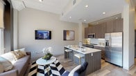 Located on the fourth floor at 1706 Washington Ave in St. Louis, Missouri, this contemporary unit offers a thoughtfully designed single-level layout with modern finishes throughout. The open-concept living and kitchen area serves as the heart of the space, featuring light hardwood-style flooring, recessed lighting, and a striking wall of large windows framed in bold dark trim that flood the room with natural light and offer sweeping views of the surrounding St. Louis cityscape. The kitchen is outfitted with textured wood-tone cabinetry, a white subway tile backsplash, quartz countertops, stainless steel appliances, and a generous island with seating — ideal for both cooking and casual dining. A long hallway connects the main living area to the private quarters, with exposed ceiling detailing adding an industrial character. The primary bedroom is bright and serene, benefiting from natural light and direct access to an en-suite bath. A second bedroom offers comfortable proportions and convenient access to a walk-in closet. The bathrooms feature clean tile flooring and wood-accented cabinetry. The overall ambiance is polished and urban, blending contemporary design with practical functionality.