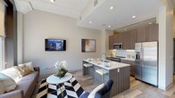 Located on the fourth floor at 1706 Washington Ave in St. Louis, Missouri, this contemporary unit offers a thoughtfully designed single-level layout with modern finishes throughout. The open-concept living and kitchen area serves as the heart of the space, featuring light hardwood-style flooring, recessed lighting, and a striking wall of large windows framed in bold dark trim that flood the room with natural light and offer sweeping views of the surrounding St. Louis cityscape. The kitchen is outfitted with textured wood-tone cabinetry, a white subway tile backsplash, quartz countertops, stainless steel appliances, and a generous island with seating — ideal for both cooking and casual dining. A long hallway connects the main living area to the private quarters, with exposed ceiling detailing adding an industrial character. The primary bedroom is bright and serene, benefiting from natural light and direct access to an en-suite bath. A second bedroom offers comfortable proportions and convenient access to a walk-in closet. The bathrooms feature clean tile flooring and wood-accented cabinetry. The overall ambiance is polished and urban, blending contemporary design with practical functionality.
