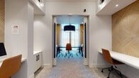 Located at 4011 Tryon Park Rd in Charlotte, NC, this thoughtfully designed business center offers a refined and productive environment for both focused individual work and collaborative meetings. The space is organized around two primary zones: an open co-working area and a private conference room.

The co-working area features extended white floating desktops set against a striking geometric wood-paneled accent wall rendered in a warm, natural tone. Ergonomic leather task chairs and built-in cabinetry with matte black hardware complete the workstation setup, creating a clean and functional aesthetic. Recessed lighting and globe wall sconces illuminate the space evenly, while plush textured carpeting adds warmth underfoot. Rich hardwood flooring in the entryway transitions seamlessly into the carpeted work zones.

The private conference room is anchored by a bold black marble-topped table surrounded by a mix of cognac leather and white upholstered task chairs. Warm amber walls and sheer floor-to-ceiling curtains frame large windows that invite natural light and provide outdoor views. A dramatic oversized drum pendant light hangs overhead, adding a sophisticated focal point. Decorative wall art adds a creative touch to the room's interior.

Together, these spaces deliver a polished, professional atmosphere well-suited for productivity and collaboration.