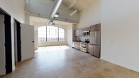 Located at 454 S San Pedro St in the heart of Los Angeles' Arts District, this single-floor loft showcases a striking industrial aesthetic with modern upgrades throughout. Soaring ceilings with exposed ductwork and structural beams set the tone, while polished concrete floors run continuously across the open-plan living space, lending a raw yet refined character.

The expansive main living area is anchored by a dramatic arched, multi-pane warehouse window that floods the space with natural light and frames views of the surrounding Los Angeles cityscape. The well-appointed kitchen features wood-grain cabinetry with dark countertops, a white tile backsplash, and a full suite of stainless steel appliances including a range, microwave, dishwasher, and refrigerator.

The sleeping area benefits from its own large grid-pane windows, continuing the theme of generous natural light. Ample closet storage is provided by dual built-in wardrobes, complemented by an in-unit stacked washer and dryer for added convenience.

The bathroom is finished with a glass-enclosed walk-in shower featuring white tile surround, matte black fixtures and hardware, a wood-toned vanity with dark countertop, and matching matte black accessories. The result is a cohesive, modern space that balances industrial heritage with contemporary comfort.