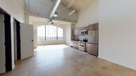 Located at 454 S San Pedro St in the heart of Los Angeles' Arts District, this single-floor loft showcases a striking industrial aesthetic with modern upgrades throughout. Soaring ceilings with exposed ductwork and structural beams set the tone, while polished concrete floors run continuously across the open-plan living space, lending a raw yet refined character.

The expansive main living area is anchored by a dramatic arched, multi-pane warehouse window that floods the space with natural light and frames views of the surrounding Los Angeles cityscape. The well-appointed kitchen features wood-grain cabinetry with dark countertops, a white tile backsplash, and a full suite of stainless steel appliances including a range, microwave, dishwasher, and refrigerator.

The sleeping area benefits from its own large grid-pane windows, continuing the theme of generous natural light. Ample closet storage is provided by dual built-in wardrobes, complemented by an in-unit stacked washer and dryer for added convenience.

The bathroom is finished with a glass-enclosed walk-in shower featuring white tile surround, matte black fixtures and hardware, a wood-toned vanity with dark countertop, and matching matte black accessories. The result is a cohesive, modern space that balances industrial heritage with contemporary comfort.