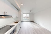 Located at 312 W Republican St in Seattle's Queen Anne neighborhood, this efficiently designed studio offers a clean, modern aesthetic throughout its single-floor layout. The open-plan kitchen and living area is anchored by light wood-look flooring and crisp white walls that maximize the sense of space. The kitchen features flat-front cabinetry in white and soft gray, a smooth cooktop, stainless steel refrigerator, microwave, undermount sink, and a combination of upper cabinets and open shelving for practical storage. The living area benefits from a large sliding window that frames views of the surrounding Seattle cityscape and fills the room with natural light. A ceiling fan adds functionality and airflow overhead. A dedicated closet with double hanging rods provides organized storage, conveniently situated near the bathroom. The bathroom continues the space's minimalist palette, featuring wood-look tile flooring, a white vanity with an undermount sink, a toilet, and a walk-in shower stall. Throughout the unit, the cohesive use of neutral tones, recessed lighting, and contemporary fixtures creates a bright, functional, and polished living environment well-suited to urban living in Seattle.