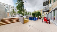 Located at 101 10th St E in Saint Paul, Minnesota, this thoughtfully designed outdoor courtyard serves as a dynamic communal gathering space nestled between several multi-story residential buildings. The grounds are richly landscaped with a diverse mix of perennial gardens, ornamental grasses, mature shade trees, and flowering plants — including vibrant black-eyed Susans, coneflowers, and hostas — that provide seasonal color and texture throughout.

Winding concrete and gravel pathways meander through the greenery, connecting distinct zones within the courtyard. A central entertainment area features a bold blue outdoor bar with bar-height seating, ideal for social gatherings. Adjacent raised stone planters with built-in greenery and comfortable lounge seating offer a relaxed setting beneath the tree canopy. Steps lead up to what appears to be a pool or water feature area, adding another layer of amenity to the space.

A lush ivy-covered living wall provides a dramatic green backdrop near the bar area, while low-profile bollard lighting lines the pathways for evening use. A dome-shaped shelter tucked into the garden offers a quiet retreat. The overall ambiance is one of an urban green oasis — well-maintained, layered with plant life, and designed to encourage both active use and peaceful relaxation amidst the surrounding cityscape.
