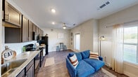 Located at 1551 Red Bud Ln in Round Rock, TX, this single-story, one-bedroom, one-bathroom unit offers a well-designed layout that maximizes every square foot. The open-concept living and kitchen area serves as the heart of the home, featuring hardwood-style flooring, recessed lighting, and a ceiling fan that enhances airflow and comfort. The kitchen is equipped with dark espresso cabinetry, a white subway tile backsplash, light granite-style countertops, a deep single-basin sink, and black appliances including a refrigerator, range, microwave, and dishwasher. A hallway connects the main living space to the private areas of the unit, and notably includes an in-unit stacked washer and dryer — a practical and convenient feature. The bedroom offers a cozy, calm atmosphere with neutral wall tones, a ceiling fan, hardwood-style flooring, and a closet. The bathroom is appointed with a full soaking tub and shower combination, clean white square tile surround, and brushed nickel fixtures. Natural light filters into multiple rooms, contributing to a bright and welcoming ambiance throughout this compact yet functional Round Rock residence.