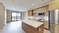 Located at 4210 Shawnee Mission Pkwy in Fairway, Kansas, this thoughtfully designed one-bedroom, two-bathroom residence offers a contemporary living experience with modern finishes throughout. The open-concept layout seamlessly connects the kitchen, dining, and living areas, creating a bright and functional common space. The kitchen is a standout feature, showcasing light wood cabinetry, a subway tile backsplash, a large center island with a white quartz countertop, and a full suite of stainless steel appliances including a French door refrigerator, electric range, built-in microwave, and dishwasher. Light wood-tone flooring runs throughout the main living areas, enhancing the airy, modern aesthetic. A sliding glass door leads to a private balcony, allowing natural light to flood the space and offering outdoor views. The carpeted bedroom is generously proportioned, featuring a ceiling fan and a large window with balcony views, and is complemented by two closets, including a walk-in. The primary bathroom is elegantly finished with large-format tile flooring, a wood-grain vanity, white quartz countertop, and a glass-enclosed walk-in shower with full-height tile surround. A dedicated laundry room with a water heater and HVAC equipment adds convenience and utility to complete this well-appointed residence.