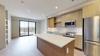 Located at 4210 Shawnee Mission Pkwy in Fairway, Kansas, this thoughtfully designed one-bedroom, two-bathroom residence offers a contemporary living experience with modern finishes throughout. The open-concept layout seamlessly connects the kitchen, dining, and living areas, creating a bright and functional common space. The kitchen is a standout feature, showcasing light wood cabinetry, a subway tile backsplash, a large center island with a white quartz countertop, and a full suite of stainless steel appliances including a French door refrigerator, electric range, built-in microwave, and dishwasher. Light wood-tone flooring runs throughout the main living areas, enhancing the airy, modern aesthetic. A sliding glass door leads to a private balcony, allowing natural light to flood the space and offering outdoor views. The carpeted bedroom is generously proportioned, featuring a ceiling fan and a large window with balcony views, and is complemented by two closets, including a walk-in. The primary bathroom is elegantly finished with large-format tile flooring, a wood-grain vanity, white quartz countertop, and a glass-enclosed walk-in shower with full-height tile surround. A dedicated laundry room with a water heater and HVAC equipment adds convenience and utility to complete this well-appointed residence.