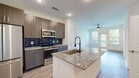 This thoughtfully designed 1-bedroom, 1-bathroom residence offers a functional and stylish open-concept floor plan. The kitchen serves as the heart of the home, showcasing granite countertops, a central island with an undermount sink and matte black spring faucet, grey shaker-style cabinetry extending to the ceiling, and a bold navy blue subway tile backsplash. A full suite of stainless steel appliances — including a French door refrigerator, electric range, and built-in microwave — completes the space. Light wood-look flooring flows throughout the main living area, which is bathed in natural light and features a ceiling fan and direct access to a private balcony through a glass-paned door. The bedroom is a comfortable retreat finished with plush carpet, a ceiling fan, and a large window with tree-lined views. A dedicated closet provides convenient storage. The bathroom carries the home's navy blue design theme forward with a full tub-shower combination, white subway wall tile accented by navy penny tile borders, and striking navy hexagonal floor tile. Clean white walls and recessed lighting throughout give the entire space a bright, modern ambiance.