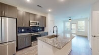 This thoughtfully designed 1-bedroom, 1-bathroom residence offers a functional and stylish open-concept floor plan. The kitchen serves as the heart of the home, showcasing granite countertops, a central island with an undermount sink and matte black spring faucet, grey shaker-style cabinetry extending to the ceiling, and a bold navy blue subway tile backsplash. A full suite of stainless steel appliances — including a French door refrigerator, electric range, and built-in microwave — completes the space. Light wood-look flooring flows throughout the main living area, which is bathed in natural light and features a ceiling fan and direct access to a private balcony through a glass-paned door. The bedroom is a comfortable retreat finished with plush carpet, a ceiling fan, and a large window with tree-lined views. A dedicated closet provides convenient storage. The bathroom carries the home's navy blue design theme forward with a full tub-shower combination, white subway wall tile accented by navy penny tile borders, and striking navy hexagonal floor tile. Clean white walls and recessed lighting throughout give the entire space a bright, modern ambiance.