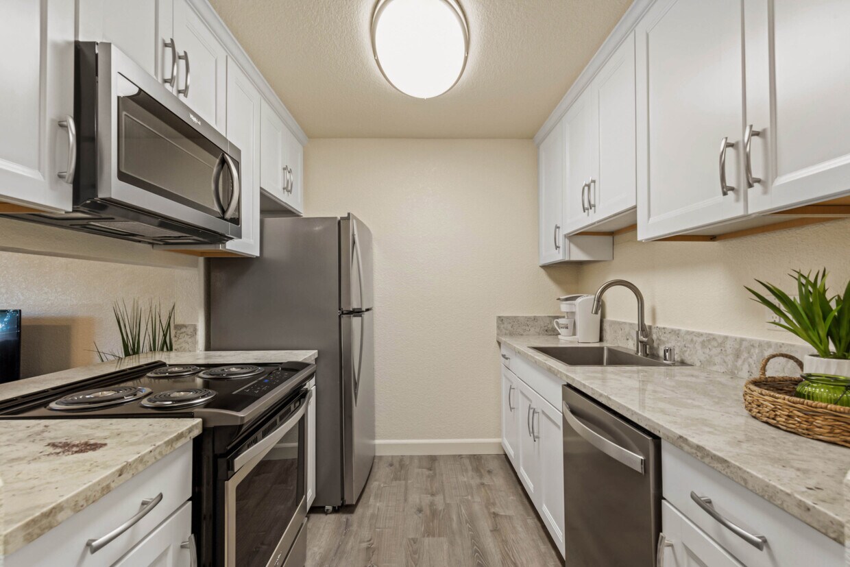 Cocina de lujo con gabinetes de cierre suave, elegantes electrodomésticos de acero inoxidable y encimeras de granito - Aggie Square Apartments