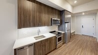 Located at 3444 South Emerson Street in Englewood, Colorado, this unit offers a thoughtfully designed single-floor layout that maximizes every square foot through clean lines and modern finishes throughout.

The kitchen is a standout feature, showcasing floor-to-ceiling wood-grain cabinetry in a rich, dark tone that creates a bold yet warm aesthetic. White quartz countertops and a classic tile backsplash provide a crisp contrast, while a full suite of stainless steel appliances — including a refrigerator, electric range, over-the-range microwave, and dishwasher — delivers a complete, functional cooking space.

The open living area flows naturally from the kitchen, finished with warm wood-look flooring that carries throughout the unit, contributing to a cohesive and inviting ambiance. Neutral white walls and recessed lighting keep the space feeling bright and airy.

The bathroom is finished to match the overall design palette, featuring wood-grain cabinetry with a white countertop vanity, a full tub-shower combo with white subway tile surround, and wood-look flooring for a consistent, polished look.

A dedicated laundry area houses a stacked full-size Whirlpool washer and dryer alongside a built-in closet rod and shelving, offering practical storage and in-unit convenience. The layout, finishes, and included amenities make this a highly functional and modern living space.