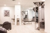 This fitness center in Woodbridge, NJ, offers a thoughtfully designed workout environment finished with light hardwood-style flooring, crisp white walls, and a drop ceiling with recessed lighting that keeps the space bright and inviting. The cardio area is equipped with multiple treadmills and elliptical trainers, each featuring individual monitor screens for an enhanced workout experience. A textured accent wall adds visual interest to this zone, complementing the clean, modern aesthetic.

The strength training area includes a cable machine with a full weight stack and various attachments, an adjustable workout bench, and a rack of dumbbells neatly arranged along a mirrored wall. The floor-to-ceiling mirror in this section visually expands the space while allowing users to monitor their form during exercises. A water fountain is conveniently positioned near the center of the room for easy access.

Framed black-and-white fitness photography decorates the walls, adding a motivational touch to the overall ambiance. A branded entryway mat bearing the Luxe identity marks the entrance, tying the space to its building. The layout is efficiently organized to support a variety of workout routines in a clean, well-maintained environment.