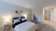 This single-floor space is designed with a clean, contemporary aesthetic that emphasizes simplicity and comfort. The bedroom serves as the central feature of the layout, offering a generously sized area finished with light wood-toned flooring that runs throughout the space, creating a warm and cohesive visual flow.

The bedroom walls are painted in soft, neutral tones, providing a calm and restful atmosphere. A window fitted with blinds allows natural light to filter in while maintaining privacy, and a wall-mounted HVAC unit ensures year-round climate control. The room offers ample space for a full furniture arrangement, including a dresser and workspace, making it as functional as it is comfortable.

A set of double doors with sleek black hardware opens to a dedicated closet, providing generous built-in storage. Adjacent to the bedroom, the en-suite bathroom continues the modern design language with light wood-style flooring, a white floating vanity with black hardware, and clean wall-mounted fixtures. Framed artwork adds a subtle decorative touch, while the overall layout makes efficient use of the available space.

Throughout the unit, the consistent use of white walls, light flooring, and black accent hardware creates a unified, modern look.