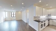 This single-floor space offers a clean, modern aesthetic defined by an open-concept layout that allows natural light and recessed lighting to illuminate every corner. The rich, dark hardwood floors run throughout, providing a warm contrast to the crisp white walls and trim that give the space a fresh, contemporary feel.

The kitchen is thoughtfully designed with bright white shaker-style cabinetry, a striking marble-patterned tile backsplash, and a bold dark countertop that anchors the space with visual contrast. Conveniently integrated into the kitchen area is an in-unit washer and dryer, adding a practical and sought-after amenity without sacrificing style.

The open living area flows seamlessly from the kitchen, creating a generous and versatile space suited for both relaxing and entertaining. A large window allows natural light to pour in, enhancing the airy ambiance. Recessed lighting installed throughout the ceiling provides consistent, modern illumination across all areas.

A connecting doorway leads to an additional room, offering flexible use as a bedroom, office, or secondary living space. The clean, neutral palette throughout ensures a timeless and adaptable interior that is move-in ready. Overall, this space combines functional design with modern finishes to deliver a polished and comfortable living environment.