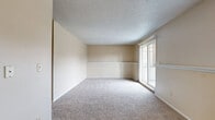Located at 894 E Old Highway 56 in Olathe, Kansas, this single-floor, 2-bedroom, 1-bathroom residence offers a practical and well-organized layout. The living room serves as the heart of the home, featuring warm neutral tones, plush carpeting, a decorative chair rail accent along the walls, a ceiling fan, and a sliding glass door that opens to a private balcony, filling the space with natural light and outdoor views. Adjacent to the living area, the combined dining and kitchen space features wood-look vinyl flooring, warm wood cabinetry, white appliances including a range and refrigerator, and access to a dedicated pantry for additional storage. Both bedrooms are carpeted and finished in soft neutral tones with textured ceilings. The primary bedroom includes a closet and natural light from a window, while the second bedroom also benefits from natural light and its own closet. A hallway connects the bedrooms to the full bathroom, which features a tub-shower combination unit. A utility room provides functional household support, and the overall layout is completed by a connecting hallway that ties all areas together efficiently. The space presents a clean, straightforward design well-suited for comfortable everyday living.