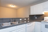 Located at 1755 20th Ave Dr NE in Hickory, NC, this two-story home offers a practical and comfortable layout spread across two well-proportioned floors. The main level features an open living area with wood-look laminate flooring, neutral-toned walls, and a textured ceiling. A row of vertical-pane windows along one wall floods the entry area with natural light and views of the surrounding neighborhood. The kitchen is conveniently situated on this floor, featuring white cabinetry with glass-front upper cabinets and dark countertops, seamlessly accessible from the main living space. A hallway on this level connects the common areas and includes bathroom access. Upstairs, the two bedrooms provide a quiet retreat. The generously sized primary bedroom is carpeted and benefits from multiple windows that invite natural light and neighborhood views. The second bedroom also features wood-look flooring and a bright window. Three bathrooms serve the home in total, each finished with white vanity cabinetry, single-basin sinks, and large mirrors. One bathroom includes a full tub-shower combination with wood-look flooring. A dedicated closet offers added storage. Throughout, textured ceilings and clean white trim create a cohesive, understated aesthetic.