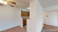 This single-floor unit at Baldwin Manor in E11 offers a practical and well-organised layout across several distinct spaces. The living area is generously proportioned, finished with warm-toned carpeting and crisp white walls. A ceiling fan provides air circulation, while a wall-mounted air conditioning unit ensures year-round comfort. Large windows fitted with blinds allow natural light to fill the room while maintaining privacy.

The kitchen follows a galley-style configuration, featuring medium-toned wooden cabinetry on both sides, laminate countertops, stone-effect tile flooring, and white appliances including a refrigerator and electric range. A pass-through opening connects the kitchen to the main living space, enhancing the sense of openness.

The bedroom is a well-sized, carpeted room with a window overlooking the exterior and access to a dedicated walk-in closet, complete with built-in shelving — a practical storage solution. 

The bathroom is finished entirely in white, with tiled flooring, a full-size bathtub with tiled surrounds, a single vanity with mirror, and a frosted window that brings in natural light while ensuring privacy. The overall aesthetic throughout is clean, neutral, and functional.