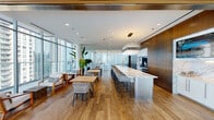 Located in Chicago's vibrant River North neighborhood, this single-floor space at 711 N State St delivers a refined, contemporary environment designed for both functionality and elegance. The open layout is anchored by wide-plank hardwood flooring that flows seamlessly throughout, unifying distinct functional zones into one cohesive setting.

The kitchen area is a standout feature, centered around an expansive marble island with seating for multiple guests. Rich walnut cabinetry lines the walls, framing a full marble backsplash that surrounds a professional-grade range and integrated appliances. A sculptural pendant light fixture adds an artistic focal point above the island.

Adjacent to the kitchen, a spacious conference and dining area accommodates a long marble-topped table surrounded by modern chairs, complemented by a large display screen mounted against the walnut wall paneling—ideal for presentations or gatherings.

The lounge area near the floor-to-ceiling glass curtain wall offers an inviting retreat, furnished with mid-century-inspired seating and lush tropical plants. A slatted wood ceiling detail adds warmth to this corner, while panoramic views of the Chicago skyline flood the space with natural light. Sheer white drapery panels provide privacy without sacrificing the airy, light-filled atmosphere throughout.