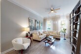 This thoughtfully designed single-floor residence offers a seamless blend of comfort and style across its well-appointed rooms. The expansive living area serves as the heart of the home, featuring wide-plank hardwood flooring, crown molding, and a ceiling fan overhead. Large windows dressed with flowing neutral drapes allow abundant natural light to pour in, offering views of lush greenery outside. A generous sectional sofa in cream anchors the space, complemented by a triptych of abstract artwork in muted greens and whites that adds a sophisticated artistic touch.

The kitchen is efficiently laid out with light maple cabinetry, granite countertops, a classic subway tile backsplash with under-cabinet lighting, and a stainless steel sink — providing both practicality and clean aesthetic appeal.

The primary bedroom is a tranquil retreat, highlighted by a striking wrought-iron four-poster canopy bed, plush carpeting, and multiple windows that bathe the room in natural light. Rich wood dressers and nature-inspired wall art complete the refined atmosphere.

The dining area near the entry features wainscoting, crown molding, and a round table with tufted upholstered chairs, creating an intimate setting. The full bathroom is finished with dark granite countertops, white cabinetry, wood-look flooring, and a soaking tub-shower combination.