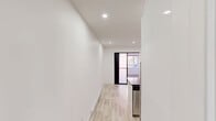 Located at 5695 Rue Saint-Jacques in Montréal's Notre-Dame-de-Grâce neighbourhood, this efficiently designed unit offers a thoughtfully laid-out single-floor plan comprising a kitchen, living room, and bathroom. The kitchen is a standout feature, showcasing high-gloss white cabinetry, dark chevron-patterned tile backsplash, and a generous central island topped with a sleek dark quartz countertop. A matte black undermount sink with an industrial-style faucet adds a refined touch, while stainless steel appliances — including a built-in oven, microwave, and refrigerator — complete the modern aesthetic. Light wood-look flooring flows seamlessly throughout the main living areas, complementing the crisp white walls and recessed lighting that keep the space feeling bright and airy. A wall-mounted mini-split unit provides climate control. The living area is clean and minimal, offering a versatile blank canvas. The bathroom is elegantly finished with floor-to-ceiling marble-style porcelain tile, a glass-enclosed walk-in shower with matte black hardware, a floating dark vanity with an integrated sink, and a sleek entry door with panel detailing. The overall design is cohesive, contemporary, and meticulously finished throughout.