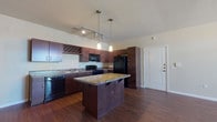 This well-appointed single-story, 3-bedroom, 2-bathroom home offers a thoughtfully designed layout that balances comfort and functionality. The open-concept kitchen is a standout feature, showcasing rich dark wood cabinetry — including a built-in wine rack — granite countertops, a center island with bar seating, and a full suite of black appliances. Track lighting and pendant fixtures illuminate the space, which flows seamlessly into the main living area over durable hardwood flooring.

The living room is bright and airy, benefiting from natural light through large windows and a glass door that opens to the exterior. A ceiling fan adds comfort to this generously sized gathering space.

Each of the three bedrooms is finished with plush wall-to-wall carpeting and ceiling fans. The bedrooms are well-sized, with at least one featuring a walk-in closet with built-in shelving and hanging rods. The rooms are connected via a hardwood-floored hallway, creating a cohesive flow throughout the home.

The bathrooms are finished with dark wood vanities, granite-style countertops, and a tub-shower combination with tiled surrounds. Overall, the home presents a clean, neutral palette with warm finishes that create a welcoming and livable ambiance.