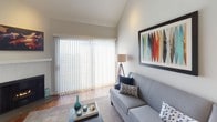 This well-designed two-floor residence offers a thoughtful layout with distinct living areas spread across both levels. The main living room immediately draws attention with its vaulted ceilings, warm hardwood flooring, and a gas fireplace framed by a textured surround. A large sliding glass door fitted with vertical blinds fills the room with natural light and provides direct outdoor access. A secondary sitting room offers a more intimate space, also featuring hardwood floors and generous window coverage.

The kitchen is outfitted with dark espresso cabinetry extending to the ceiling, stainless steel appliances including a refrigerator, range, microwave, and dishwasher, and a light-toned countertop that creates a striking contrast. Recessed lighting and rich hardwood floors complete the contemporary aesthetic.

The primary bedroom is carpeted and features a sliding glass door, plantation shutters, recessed lighting, and direct access to an en suite bathroom. The bedroom also includes a built-in closet with integrated drawer storage. A second bedroom provides additional flexible living space.

The bathrooms are finished with clean, modern fixtures. One features a dark vanity paired with a glass-enclosed tub-shower combo, while another showcases a frameless glass walk-in shower with a multi-function panel system and rainfall showerhead, all set against bright, light-toned tile surfaces.