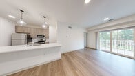 Located at 2967 Route W in Saugerties, NY, this single-floor residence offers a clean, contemporary design throughout. The open-concept living and kitchen area is anchored by light hardwood-style flooring and recessed lighting, creating a bright and airy atmosphere. The kitchen is well-appointed with light wood cabinetry, stainless steel appliances including a refrigerator, range, and microwave, and a generous white quartz peninsula with an integrated sink and stylish pendant lighting overhead. A sliding glass door in the living area provides access to an outdoor balcony and allows natural light to flow in. The bedrooms feature plush wall-to-wall carpeting and large windows with blinds that frame views of the surrounding greenery, lending each room a calm, comfortable feel. The bathrooms are finished with wood-style flooring, clean white fixtures, and brushed nickel hardware accents. The primary bathroom includes a vanity with wood-toned cabinetry and convenient access to a walk-in closet. A dedicated laundry area houses a stacked washer and dryer unit alongside a water heater, adding practical convenience to the home. Overall, the space presents a fresh, move-in-ready environment with modern finishes and a cohesive neutral palette throughout.