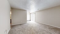 Located at 3210 SW Twilight Ct in Topeka, Kansas, this single-floor residence offers a practical and comfortable layout with a consistent neutral color palette throughout. The living area is generously sized, featuring plush wall-to-wall carpeting, a ceiling fan, textured ceilings, and a sliding glass door dressed with vertical blinds that allows natural light to fill the space. The galley-style kitchen is efficiently designed with dual rows of dark upper cabinetry and white lower cabinets, laminate wood-look flooring, a double stainless steel sink with granite-look countertops, and white appliances including a coil-top range and refrigerator. The bedrooms are carpeted and well-proportioned, with neutral walls and textured ceilings. One bedroom features a walk-in closet with built-in shelving, as well as an additional door providing extra storage or access options, along with a window offering outside views. The bathroom is cleanly appointed with a large vanity mirror, a wide single-basin sink, and white fixtures. Throughout the home, white baseboards provide clean transitions between walls and flooring, contributing to the overall bright and tidy character of the space.