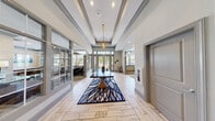 Located at 100 Legacy Way in Yorktown, Virginia, this sophisticated single-floor clubhouse is designed to impress with refined architectural details and a cohesive, upscale aesthetic throughout. The grand entrance foyer sets the tone immediately, featuring soaring tray ceilings adorned with elegant crown molding, a statement pendant chandelier, and light herringbone-patterned tile flooring. Floor-to-ceiling glass panels and French doors flood the space with natural light and offer views of the surrounding greenery.

The lounge area is a standout, anchored by a bold blue coffered accent wall with decorative paneling, plush sectional seating, and stylish gold-accented furnishings beneath an orb chandelier. Adjacent to the lounge, a spacious game room features a full-size billiard table, bar-height seating, a fireplace, and generous windows with garden views.

A fully equipped community kitchen includes a large island with dark quartz countertops, pendant lighting, stainless steel appliances, a coffee station, and a built-in beverage cooler, making it ideal for gatherings. The business center offers a conference table, individual workstations, computer terminals, and abundant natural light — a functional and professional workspace. Throughout, herringbone flooring, recessed lighting, and curated artwork tie every area together seamlessly.