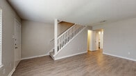 This two-story home in Houston's 77079 zip code offers a practical and comfortable layout across two floors. The main level features warm hardwood-style flooring throughout the living areas, a white-railed staircase connecting both floors, and a functional kitchen equipped with stainless steel appliances including a refrigerator and dishwasher, white cabinetry, and ample counter space. A dedicated laundry room with a full-size top-load washer and dryer adds everyday convenience. Two living areas provide flexible space for entertaining or relaxing, and neutral beige tones throughout create a clean, cohesive aesthetic. The upper floor houses the three bedrooms, each finished with either plush carpet or hardwood-style flooring. The spacious primary bedroom features a ceiling fan, a large closet with built-in shelving, and a sliding glass door that lets in abundant natural light and offers outdoor views. Additional bedrooms also benefit from natural light via sliding glass doors with vertical blinds. Three full bathrooms serve the home, including one with a tiled tub-shower combination. The overall ambiance is bright, neutral, and move-in ready, suited for comfortable everyday living.
