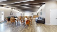 Located at 900 Mickley Road in Whitehall, PA, this single-floor communal space offers a welcoming and functional layout designed to accommodate both social gatherings and everyday use. The space is defined by its distinctive exposed wooden beam ceiling, which runs the length of the room and adds a rustic, architectural character that contrasts with the warm, neutral-toned walls and wood-look flooring throughout.

The main living area is generously proportioned, providing ample room for multiple seating arrangements. A dining zone features several round wooden tables surrounded by classic Windsor-style chairs, creating a casual yet organized setting suited for group gatherings or shared meals. Adjacent to the dining area, a lounge section is furnished with leather sofas and accent chairs, offering a comfortable retreat for relaxation.

A built-in kitchen area is integrated into the space, equipped with stainless steel appliances including a refrigerator and range, along with a center island and cabinetry — supporting food preparation and serving needs. Near the entry, a smaller seating nook with upholstered chairs and a side table provides an inviting transition zone. Windows along the walls allow natural light to filter in, enhancing the bright and open ambiance of the space.