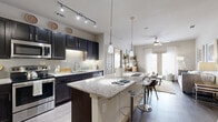 This single-floor, 2-bedroom, 2-bathroom residence offers a thoughtfully designed open-concept layout that seamlessly connects the kitchen, dining, and living areas. The kitchen is a standout feature, showcasing dark espresso cabinetry with under-cabinet lighting, granite countertops, a tile backsplash, stainless steel appliances, and a large center island with bar seating illuminated by pendant lighting. Track lighting overhead adds a modern touch. The living room is bright and welcoming, with large French doors that invite abundant natural light and provide outdoor access, complemented by a ceiling fan and wood-style flooring. Both bedrooms are carpeted and feature ceiling fans, generous natural light from large windows, and access to dedicated closets — including a spacious walk-in closet with built-in shelving. Each bathroom mirrors the kitchen's design aesthetic, featuring granite-topped dark vanities, framed mirrors, and wood-style flooring. One bathroom includes a shower-tub combination, while the other offers a streamlined layout adjacent to a bedroom. Two closets provide ample storage throughout the home. The overall ambiance is modern and cohesive, with a neutral color palette and upscale finishes creating a clean, comfortable living environment.
