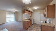 Unit R201 is a single-floor residence designed with a practical, open layout that connects the kitchen and living areas seamlessly. The kitchen is equipped with warm oak-toned cabinetry, a white electric range, refrigerator, dishwasher, and a double-basin sink set into a laminate countertop. A pass-through window opens the kitchen directly to the living area, enhancing the sense of openness and allowing natural light to flow between spaces. The living area features plush carpeting, a ceiling fan with light fixture, and a sliding glass door that leads to a private balcony, providing outdoor access and natural light.

The bedrooms are carpeted and each includes a ceiling fan with lighting. One bedroom benefits from a window with exterior views, contributing additional natural light. The unit includes two bathrooms: a full bath with a tub-shower combination, single-sink vanity with wood cabinetry, and wood-look flooring; and a second bathroom featuring a standalone shower stall with a frosted glass door and wood-look flooring. Throughout the unit, neutral wall tones, white trim, and consistent finishes create a cohesive and functional living space.