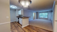 Located at 100 Preston Woods Trail in Sandy Springs, Georgia, this single-floor residence offers a well-designed, open-concept layout that balances comfort and functionality. The living area is generously proportioned, finished with plush wall-to-wall carpeting, crown molding, and neutral-toned walls that create a bright, welcoming atmosphere. Large windows with blinds throughout allow ample natural light to fill each room while offering views of surrounding greenery.

The kitchen is a standout feature, equipped with white shaker-style cabinetry, dark granite-look countertops, stainless steel appliances — including a refrigerator, range, microwave, and dishwasher — and warm hardwood flooring. A peninsula counter connects the kitchen to the dining area, which is highlighted by a pendant light fixture and chair-rail molding detail.

The bedrooms are carpeted and spacious, with one room featuring a walk-in closet. The bathroom includes a soaking tub with a tiled shower surround and chrome fixtures. A dedicated in-unit laundry room accommodates a full-size washer and dryer set with overhead shelving for added storage. The overall design is clean, neutral, and move-in ready, offering a comfortable living environment in the heart of Sandy Springs.