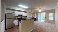Located at 2705 E Lookout Dr in Garland, Texas, this three-story residence offers a thoughtfully organized layout spread across multiple levels, connected by carpeted stairs with clean white railings. The entry level includes an attached garage with an automatic opener, providing secure, convenient parking and additional storage space.

The main living level showcases an open-concept design where the kitchen flows seamlessly into the living area. The kitchen features white cabinetry, dark speckled countertops, stainless steel appliances including a refrigerator and microwave, and a peninsula that serves as a natural divider between cooking and living spaces. Wood-style flooring grounds the kitchen, while the adjoining living area transitions to plush carpet. A ceiling fan with a light fixture enhances comfort, and a sliding glass door draws in natural light and provides outdoor access.

Upper-level bedrooms benefit from vaulted ceilings and large windows that invite abundant natural light. The primary bedroom includes a generously sized walk-in closet with built-in shelving and carpeted floors. Bathrooms are finished with white tile surrounds, tub-shower combinations, wide vanity countertops with speckled finishes, and ample cabinet storage, contributing to a clean, functional aesthetic throughout.
