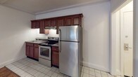 This single-floor unit offers a functional and comfortable layout with a variety of notable interior details throughout. The main living area is spacious and open, featuring warm hardwood-style flooring that flows seamlessly through the space. Crown molding frames the room, adding a classic touch, while a textured ceiling provides additional character. White walls keep the area bright and neutral, offering a versatile canvas for any style.

The kitchen is well-appointed with rich, dark wood cabinetry offering generous storage, dark granite-style countertops, and a full suite of stainless steel appliances including an electric range with overhead ventilation, a full-size refrigerator, and a sink. Light tile flooring in the kitchen provides a clean, practical surface that complements the cabinetry.

The bathroom features a retro-inspired design with distinctive terracotta-toned wall tiles surrounding a full shower and tub combination. A window above the tub allows for natural light, while classic mosaic-style tile flooring and a drop-in ceiling complete the look.

Additional highlights include a closet accessible from the living area, a tiled entryway near the front door, and well-maintained white trim and baseboards throughout, contributing to a clean and cohesive aesthetic across the entire space.